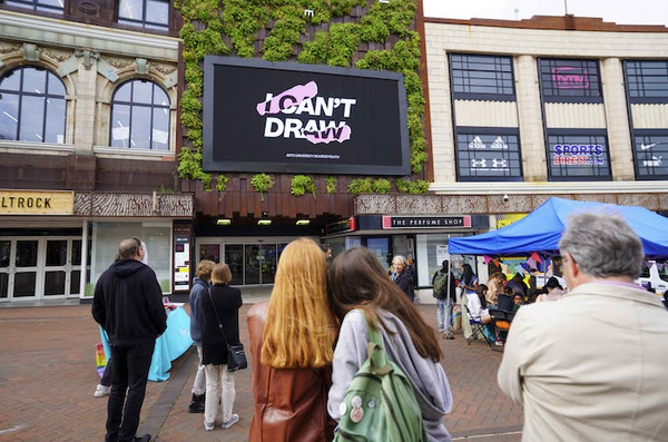 Crowd of people look at a big screen display with logo of Art Exhibition 