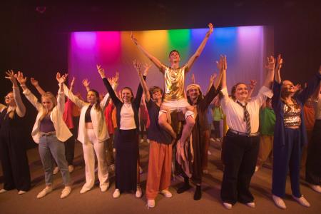Student cast members of Joseph and the Amazing Technicolor Dreamcoat on stage, holding aloft Joseph